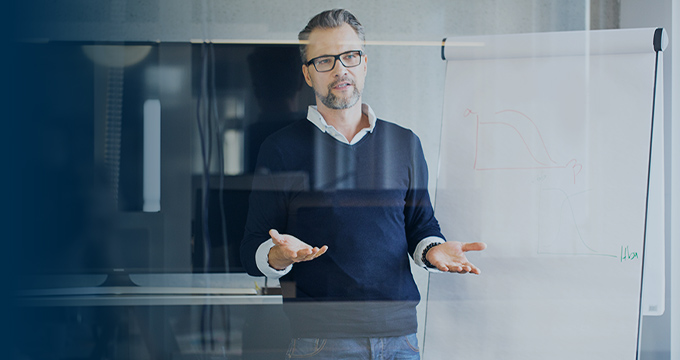 A man standing in front of a window with his hands out as he talks