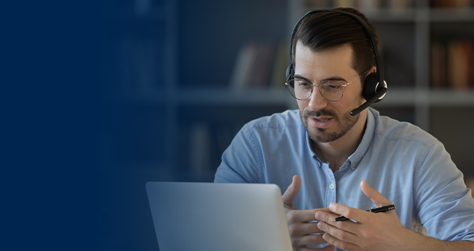 A man with a headset on talking in front of a computer