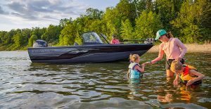 A woman with two kids in a lake while a man is sitting in a boat smiling behind them